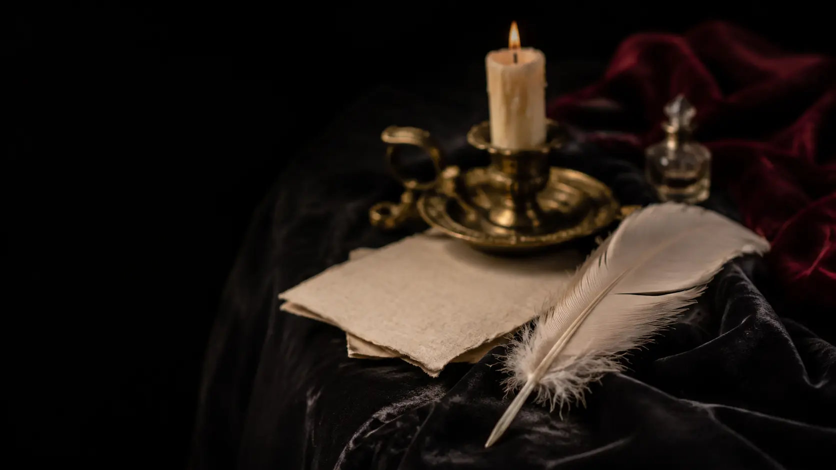 Pluma marfil sobre terciopelo negro junto a un papel escrito a mano y un candelero de bronce antiguo.